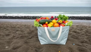 A eco-friendly organic cotton tote bag overflowing with colorful fruits and vegetables, standing on a beach against a backdrop of a polluted ocean with plastics.